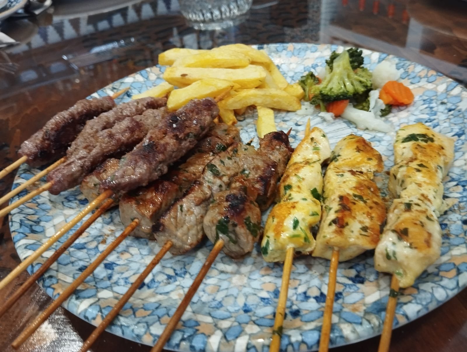 Meat and chicken skewers with fries and vegetables on a blue plate